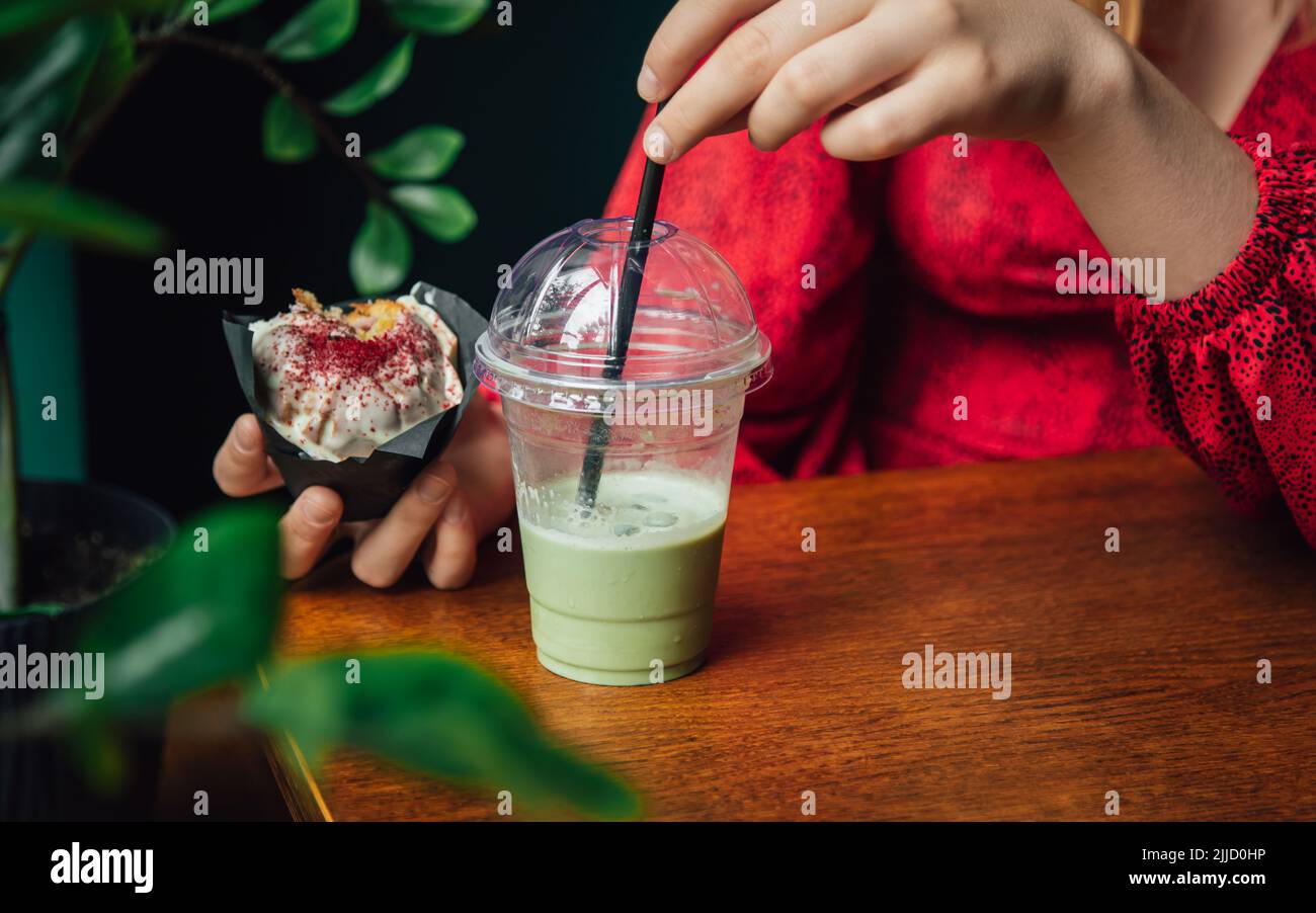 Latte au matcha glacé et gros gâteau dans un café entre les mains des femmes. Banque D'Images