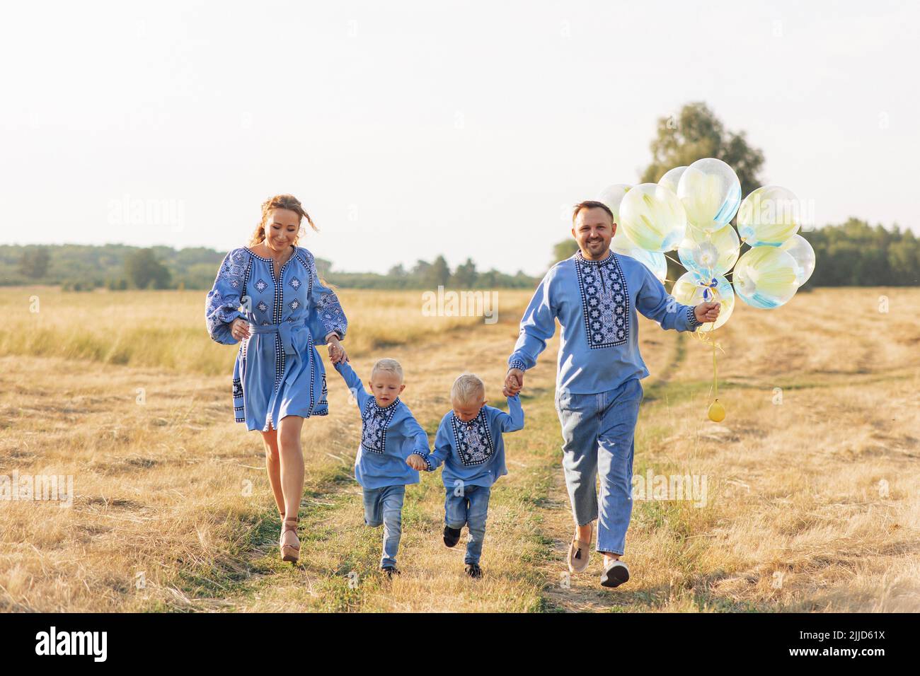 Parents heureux avec deux leurs fils jumeaux ont plaisir et courir sur la prairie avec des ballons d'air. Ils sont habillés de chemises nationales ukrainiennes brodées. Fermer Banque D'Images