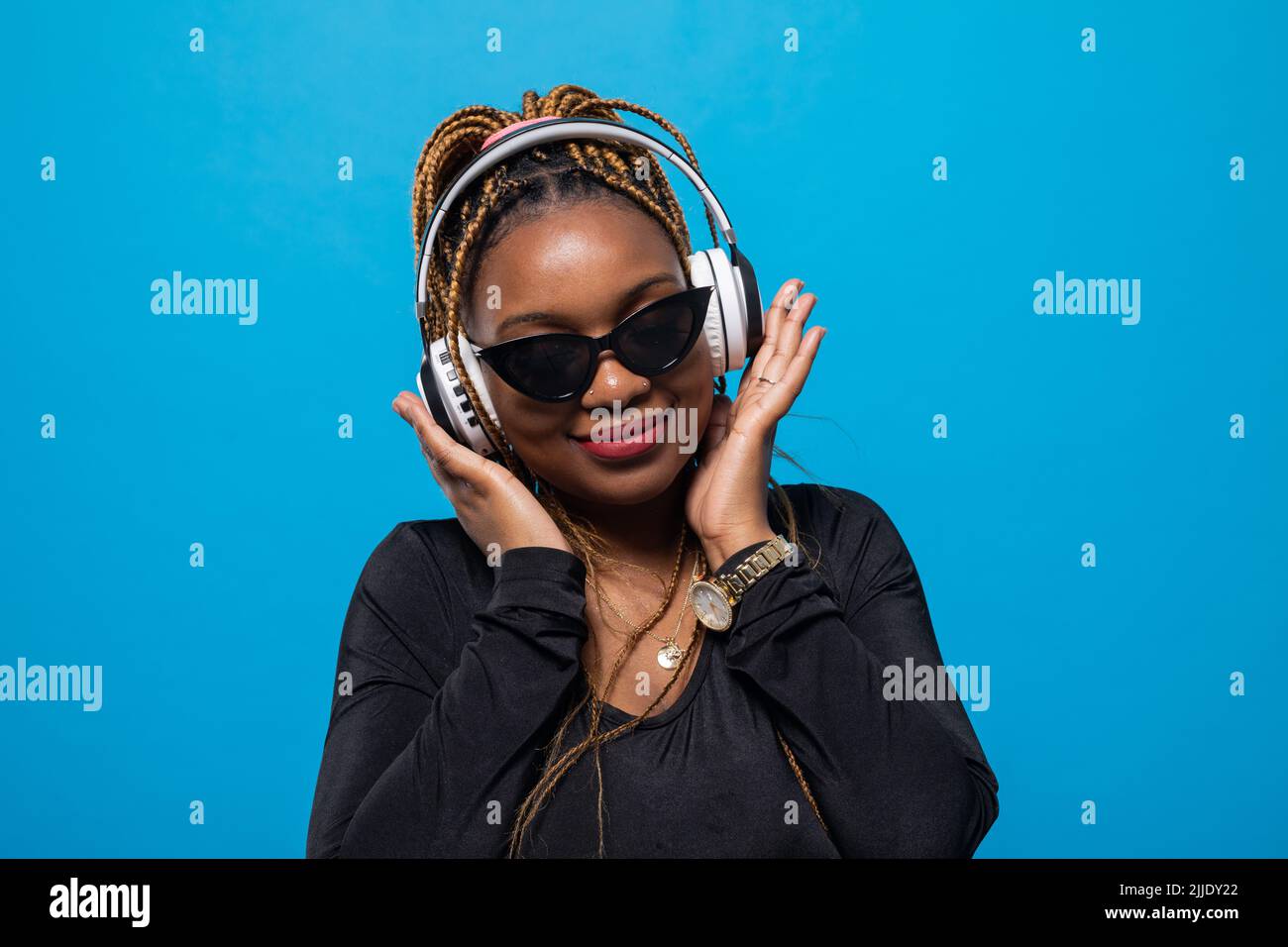 Une femme portant des lunettes de soleil regarde l'appareil tout en écoutant de la musique. Banque D'Images