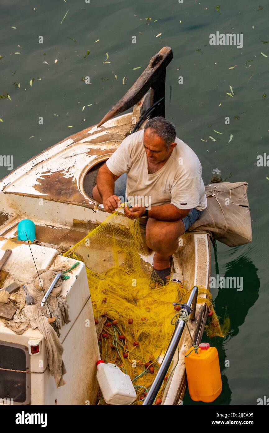 pêcheur grec sur l'île de crète en train de faire des filets sur son bateau dans un port à la lumière du soir, pêcheur grec en bateau en train de réparer des engins pour demain Banque D'Images