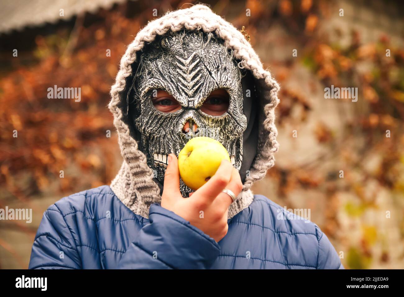 Recentrer le portrait des gens d'Halloween. Personne dans le sombre masque de couche debout sur la nature automne de fond manger pomme. Halloween horreur. Fantôme du crâne. Sinistre r Banque D'Images