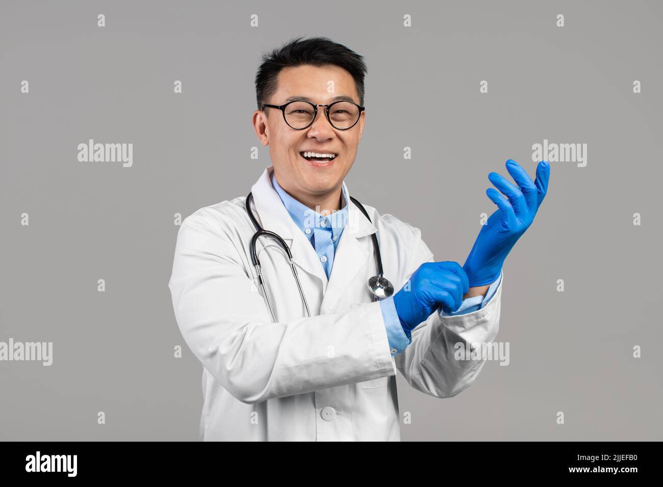 Gai millennium chinois mec docteur en manteau blanc, lunettes avec stéthoscope porte des gants en caoutchouc Banque D'Images