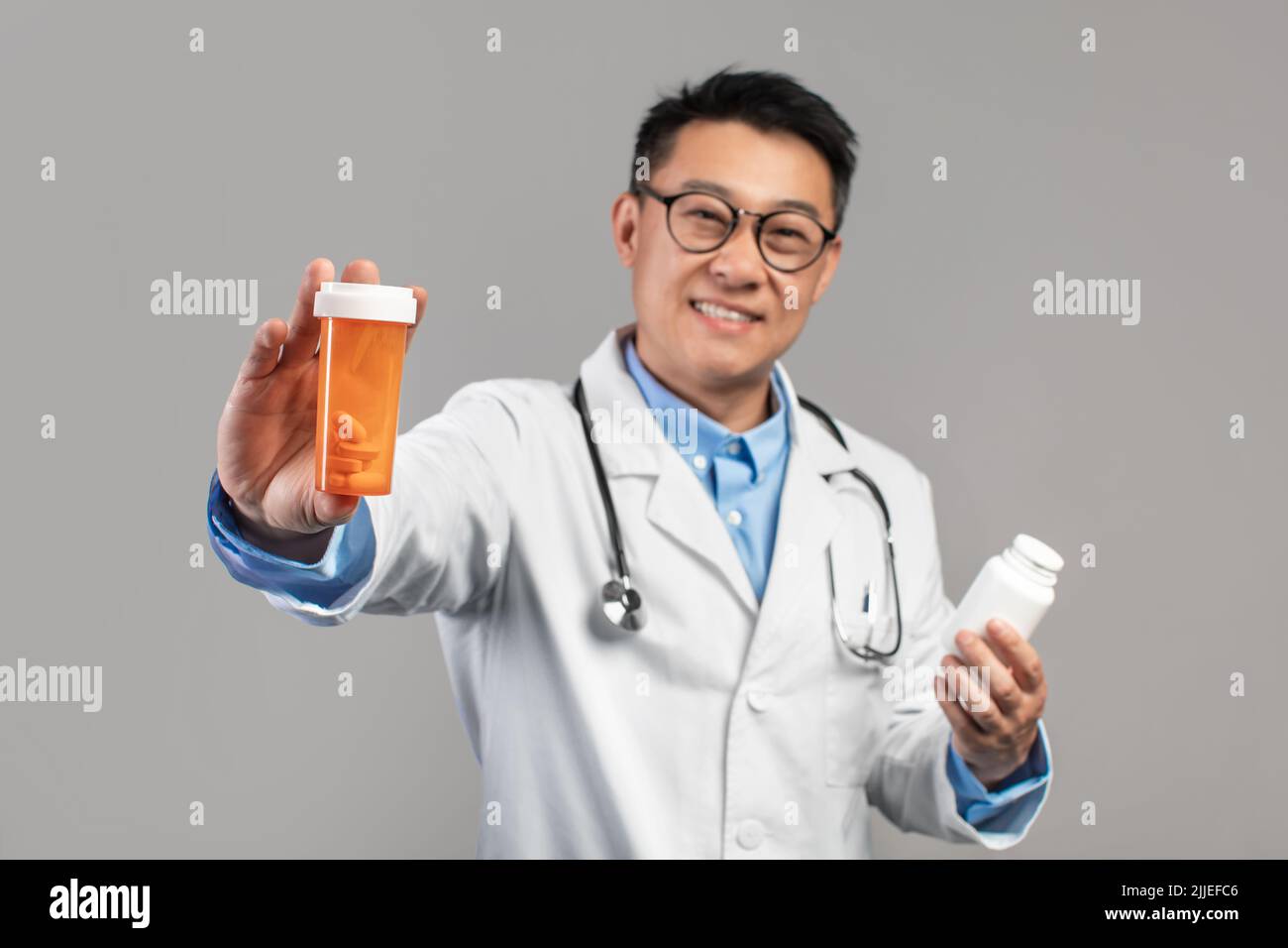 Gai adulte asiatique gars docteur en manteau blanc, des verres avec stéthoscope montrer des bocaux avec des pilules Banque D'Images