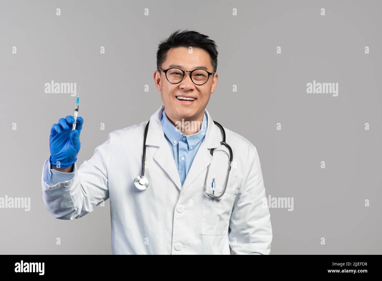 Joyeux homme japonais mature médecin en manteau blanc, verres, gants de protection tiennent la seringue Banque D'Images