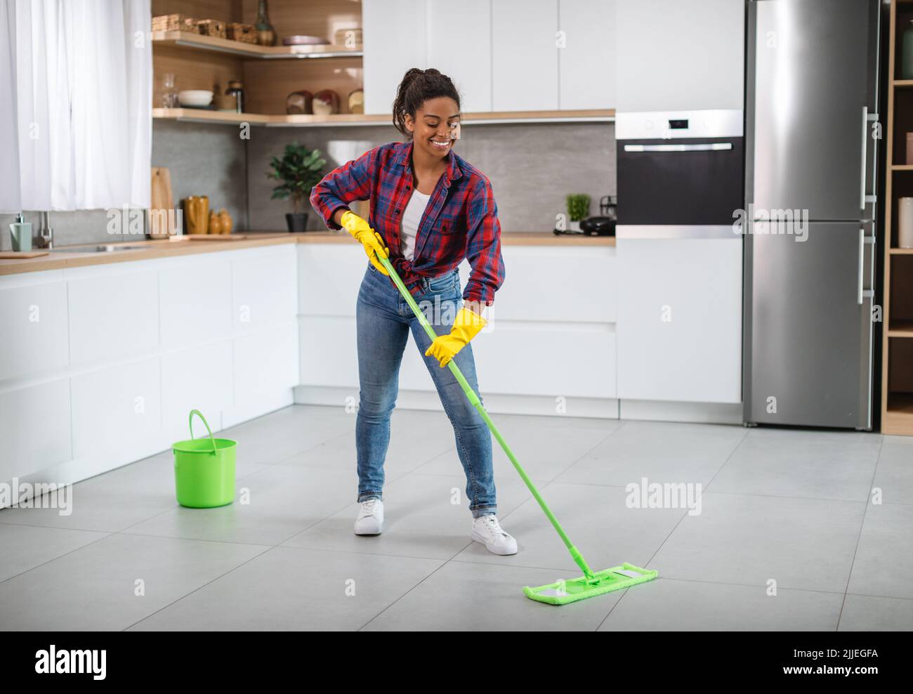 Femme au foyer noire millénaire gaie dans des gants en caoutchouc avec mop lave le sol, aime le nettoyage Banque D'Images