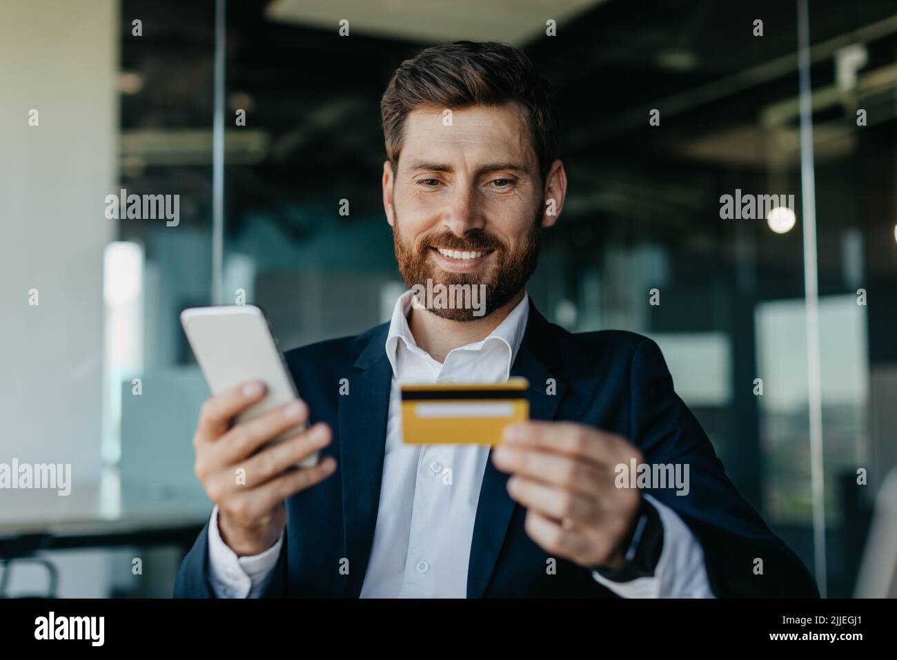 Concept de banque en ligne. Happy caucasiens directeur général faire le paiement en ligne sur smartphone, assis dans le bureau Banque D'Images