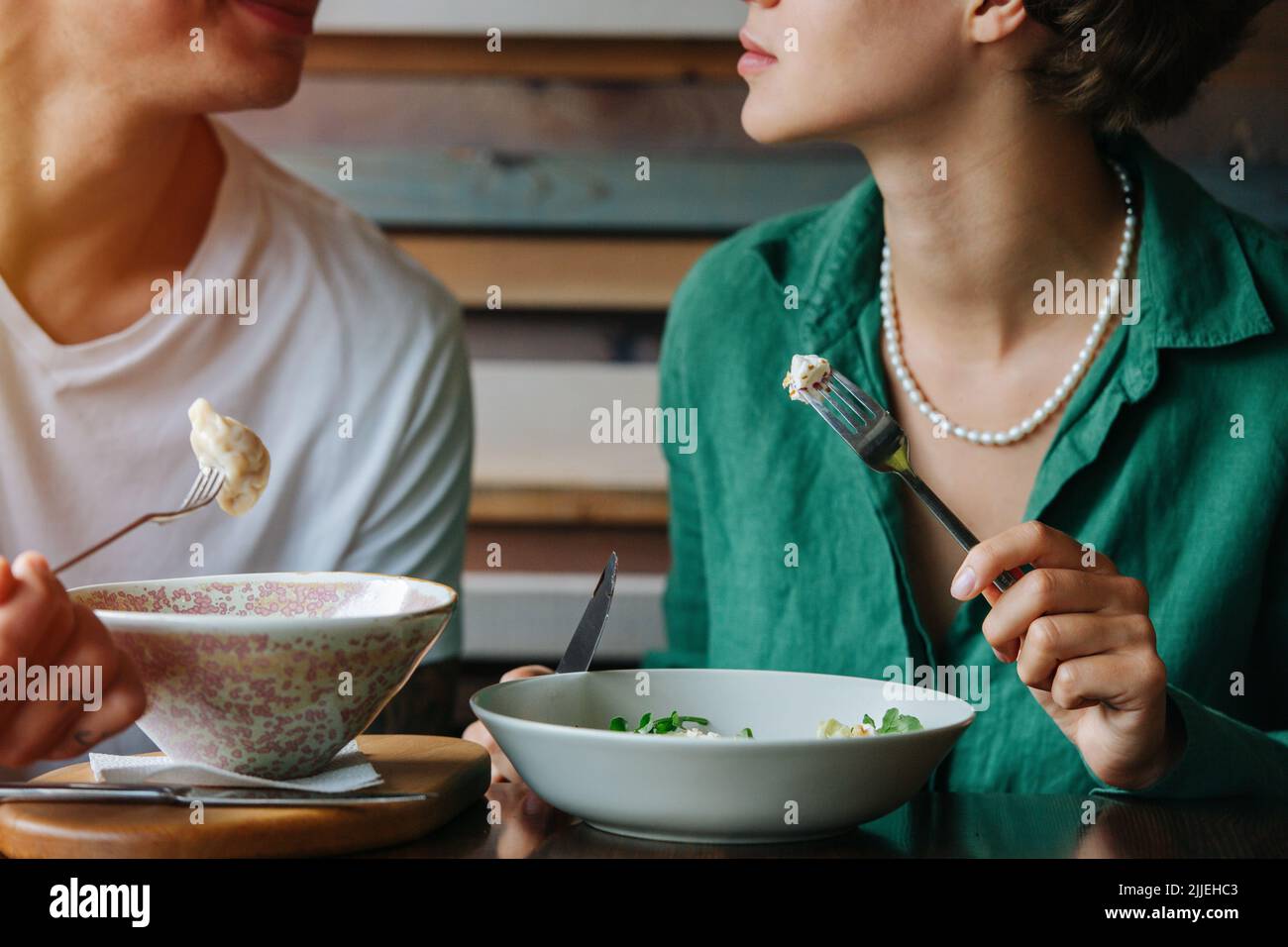 Image rognée d'un couple assis dans un café à côté, regardant l'un l'autre. Avoir de la nourriture sur leurs fourchettes. Face inférieure, lèvres et menton uniquement. Banque D'Images