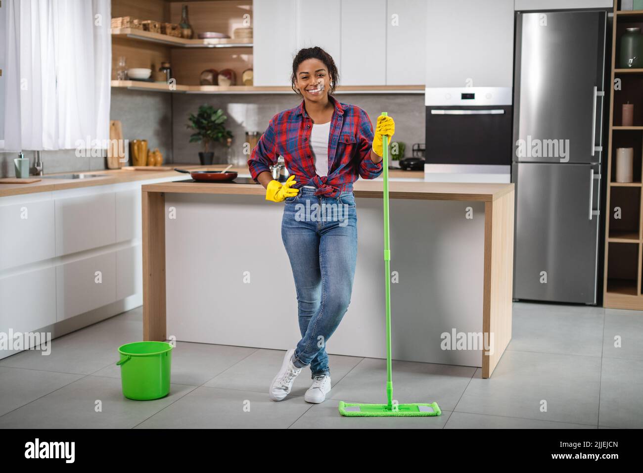 Femme afro-américaine souriante millénaires femme au foyer dans des gants en caoutchouc avec mop lave le sol, aime le nettoyage Banque D'Images