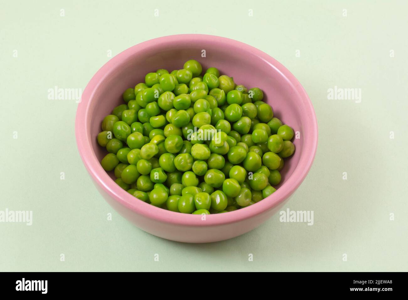 Petits pois verts frais dans un bol rose sur fond vert clair Banque D'Images