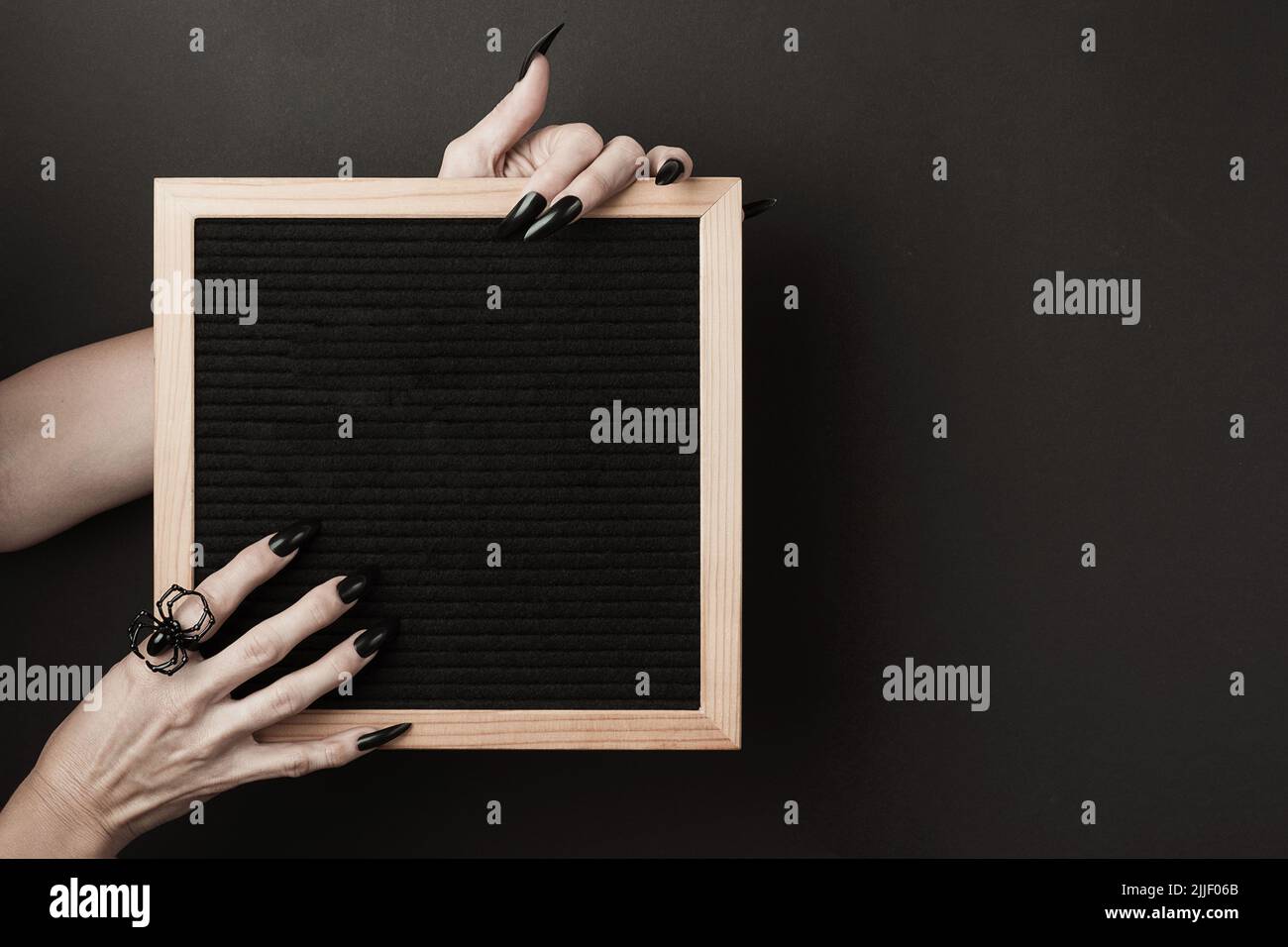 Maquette d'Halloween. Tableau de lettres dans les mains avec de longs ongles noirs et une bague d'araignée sur fond noir. Vue avant. Banque D'Images