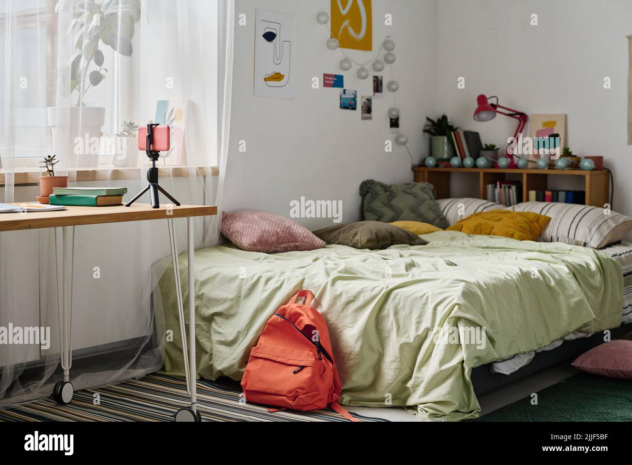 Image horizontale de la chambre des adolescents avec lit confortable et table avec smartphone sur trépied Banque D'Images