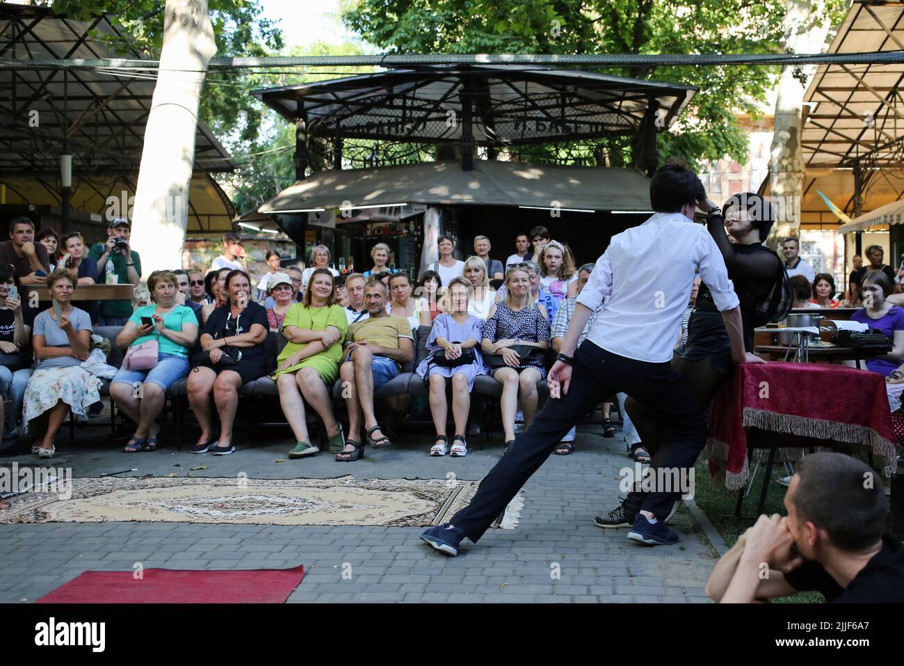 Le public regarde comme acteurs de théâtre exécuter "Odessa, je vous aime" sur le marché du livre à Odessa. La performance "Odessa, je t'aime" raconte des histoires de la vie des habitants d'Odessa avec sa couleur caractéristique et son humour. La représentation a été mise en scène par les acteurs du Théâtre n° 7 et jouée à l'extérieur sur le marché du livre. Le but de cette performance est de recueillir des dons pour les besoins de défense aérienne. Banque D'Images