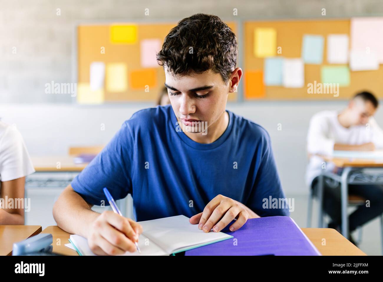 Élève de sexe masculin étudiant à un bureau dans une salle de classe scolaire Banque D'Images