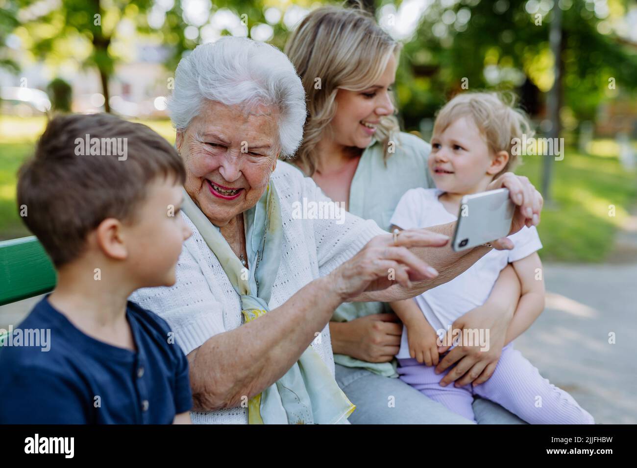 Une grande grand-mère qui prend le selfie avec sa petite-fille et ses enfants lorsqu'elle est assise au parc en été. Banque D'Images