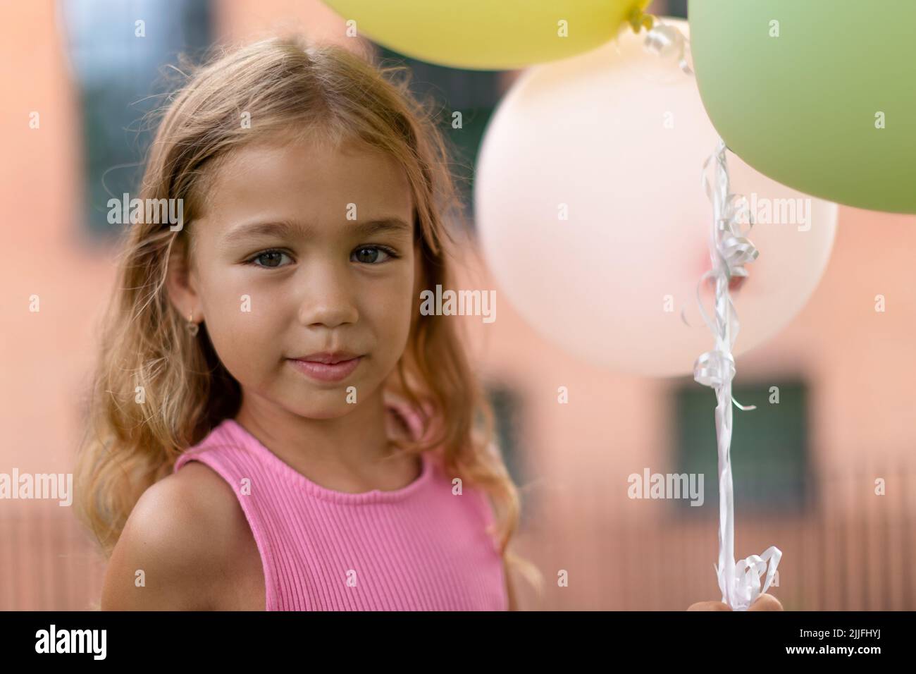 Petite fille blonde posant avec des balons dans la ville et regardant la caméra. Banque D'Images