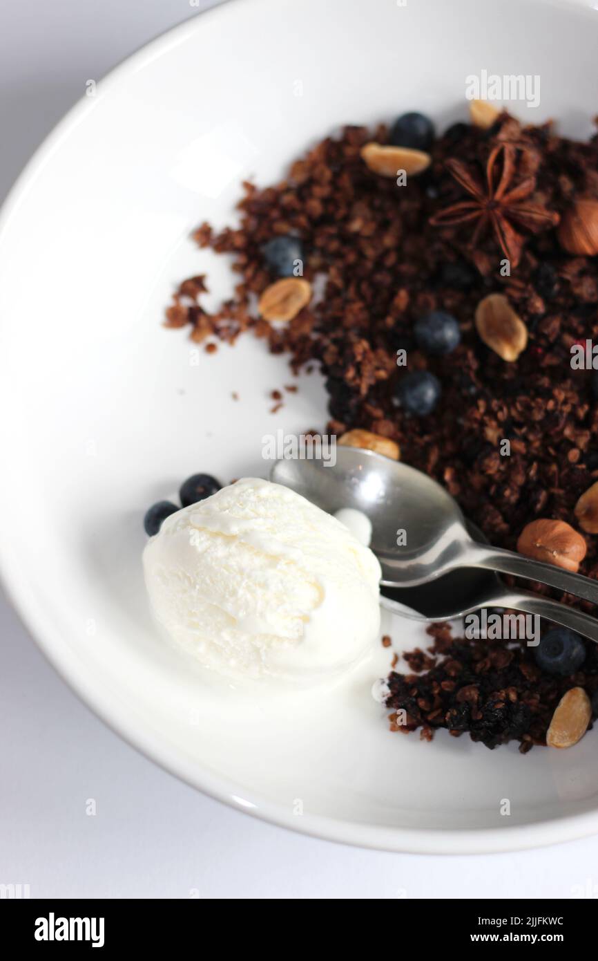 Une cuillère de glace à la vanille accompagnée d'un dessert de granola aux myrtilles et de noix. Banque D'Images