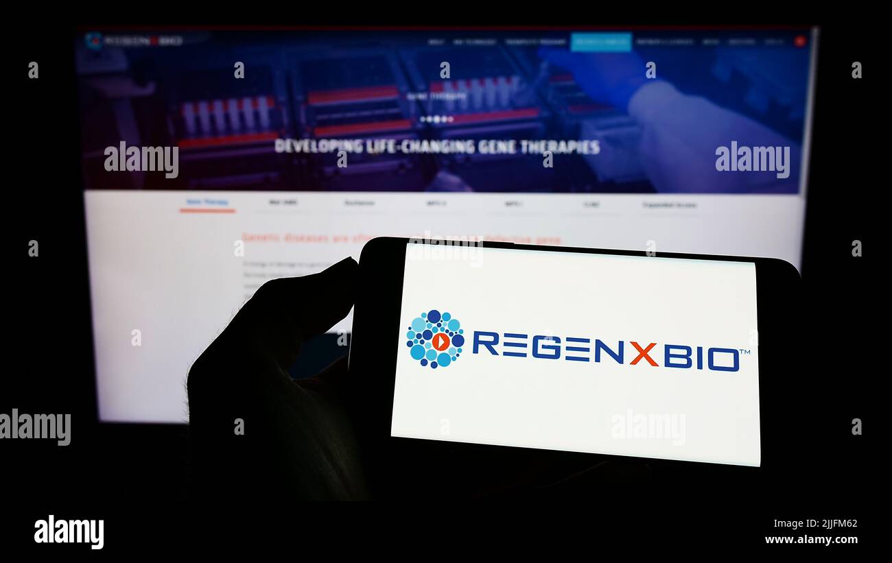 Personne tenant un téléphone portable avec le logo de la société américaine de biotechnologie Regenxbio Inc. À l'écran devant la page Web des affaires. Mise au point sur l'affichage du téléphone. Banque D'Images