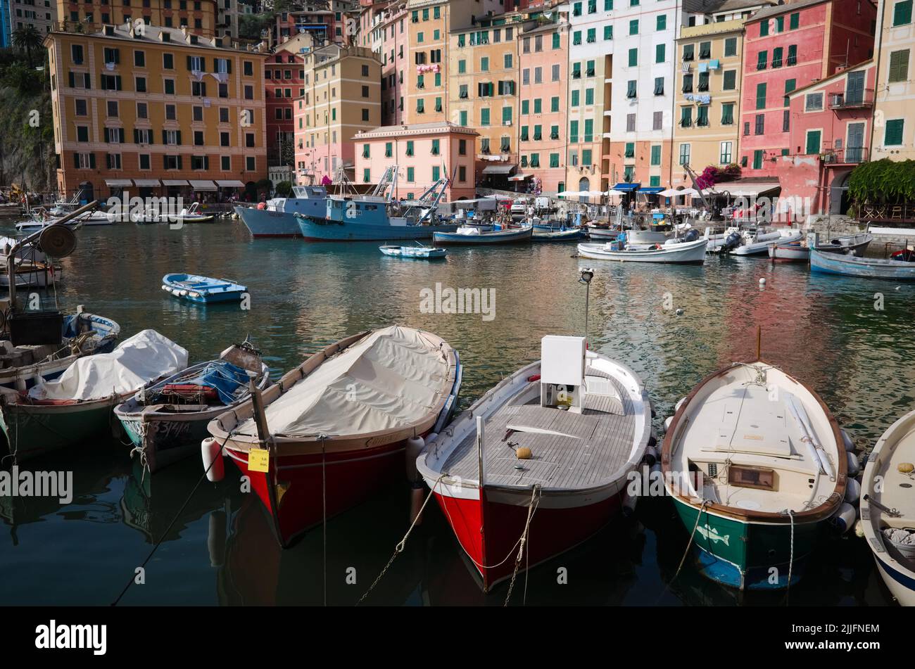 Camogli, Italie - juin 2022 : petits bateaux amarrés en rangée dans le port. Bateaux de pêche et maisons à volets dans un style typiquement italien en arrière-plan. Banque D'Images