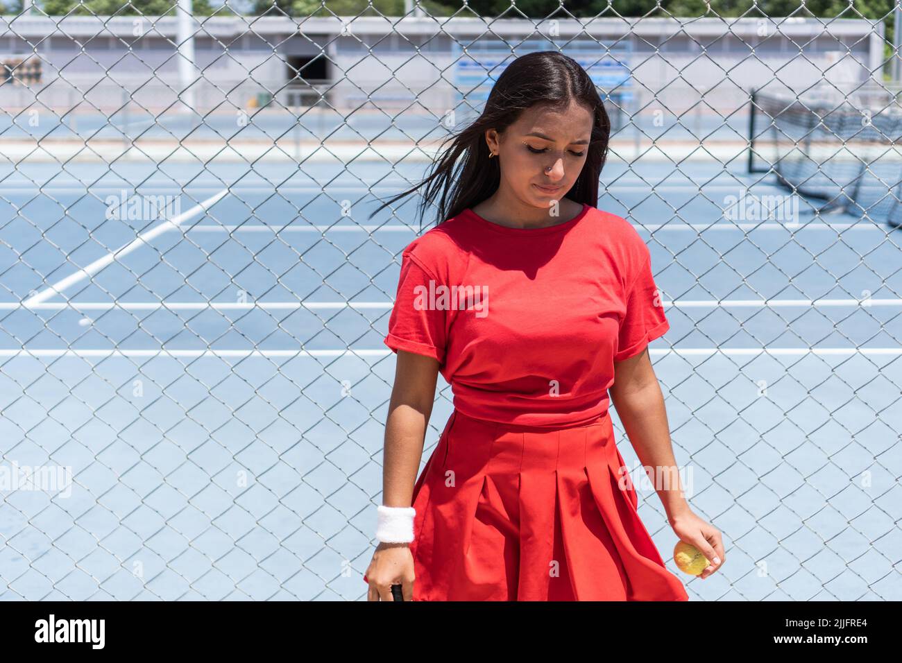 Athlète avec raquette et balle debout près de la clôture du court de tennis pendant la pause dans l'entraînement. Banque D'Images