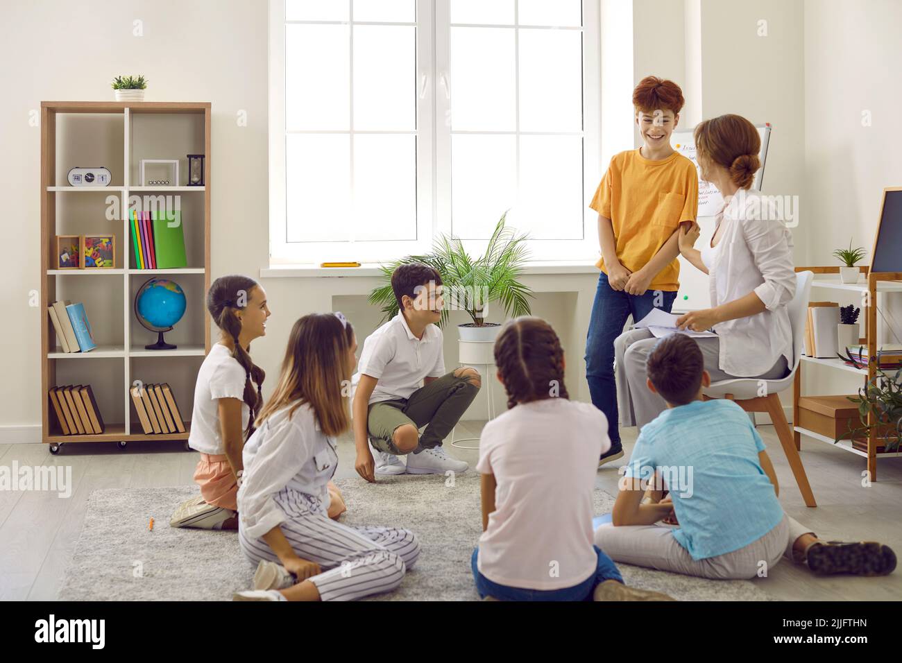 Groupe d'élèves heureux assis sur le plancher pendant le cercle de temps avec leur enseignant Banque D'Images