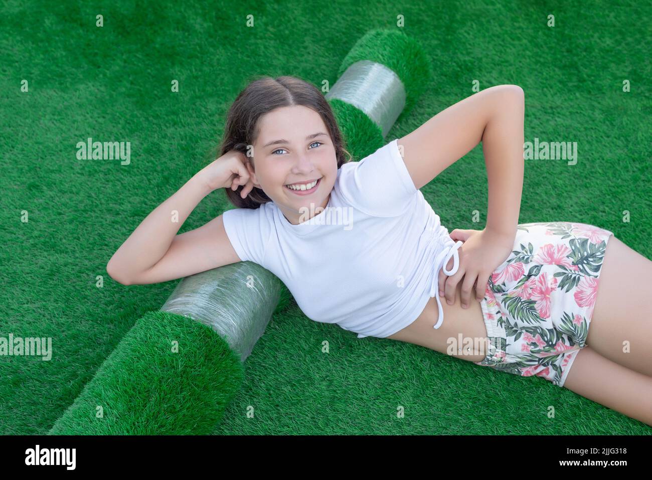 Jeune fille caucasienne souriante couché sur un nouveau rouleau de gazon artificiel. Herbe artificielle agréable prête à pondre Banque D'Images