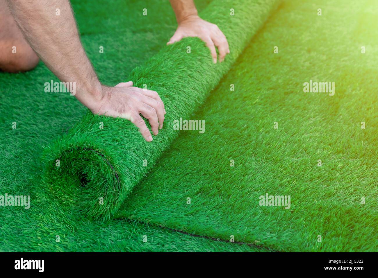 Accent sélectif sur les mains d'un homme qui déroulent un rouleau de gazon artificiel. Pose facile d'herbe verte artificielle Banque D'Images