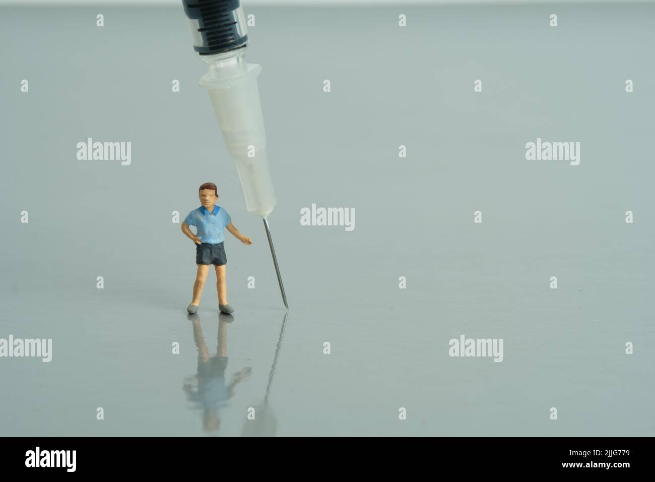 Photographie miniature de personnage de jouet de personnes. Concept de vaccination des enfants. Un garçon debout à côté de la seringue invite à se faire vacciner. Photo d'image Banque D'Images