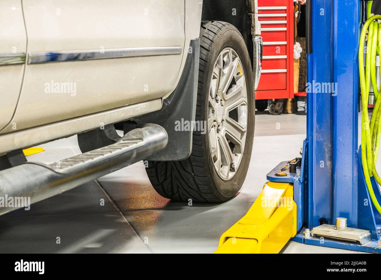 Gros plan de la roue massive d'un pick-up blanc debout sur le support de levage avant le début du contrôle. Atelier d'entretien automatique à l'arrière Banque D'Images