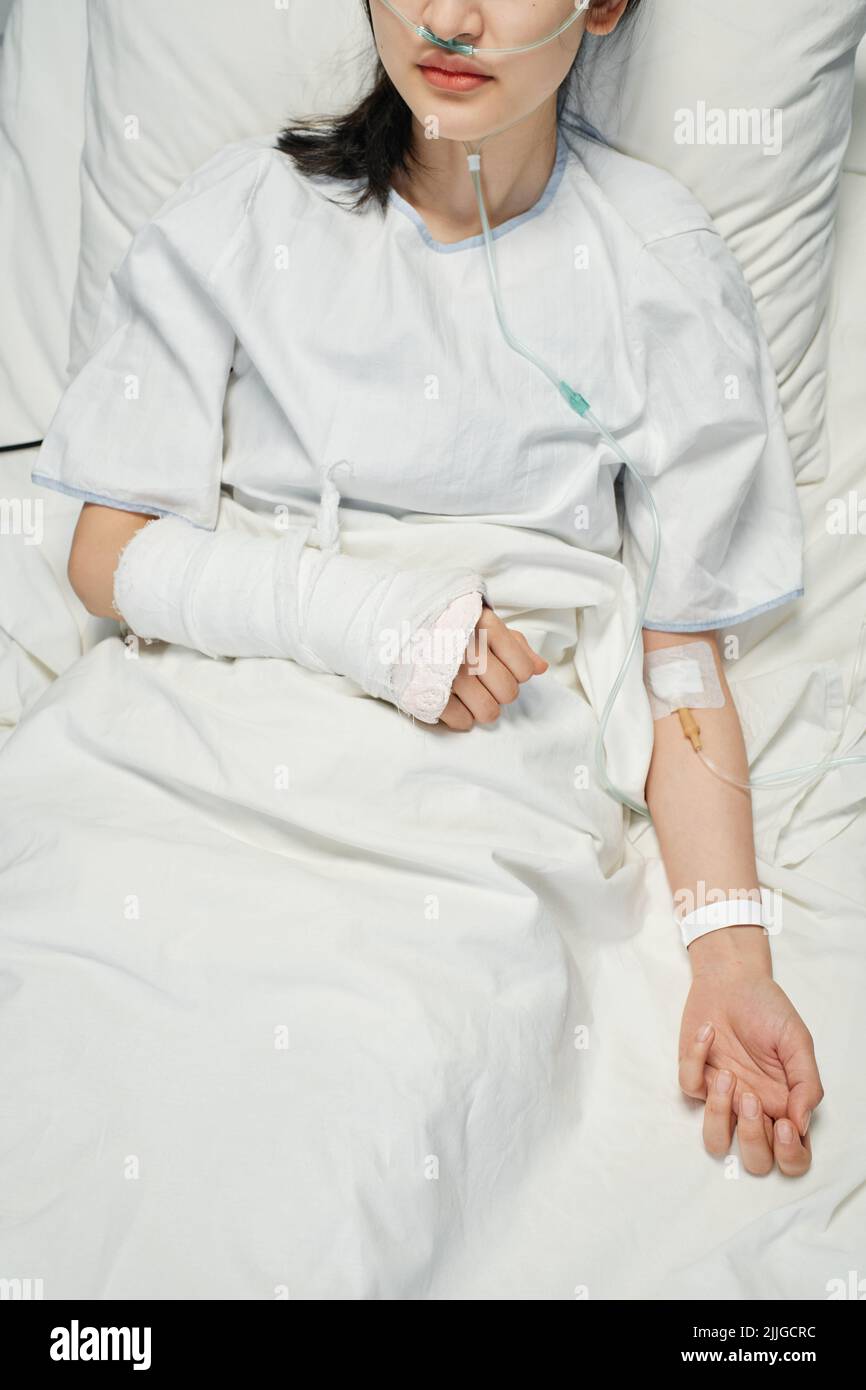 Tir vertical à grand angle d'un jeune patient asiatique avec un bras cassé en fonte recevant des médicaments ou des fluides nutritifs par voie intraveineuse Banque D'Images