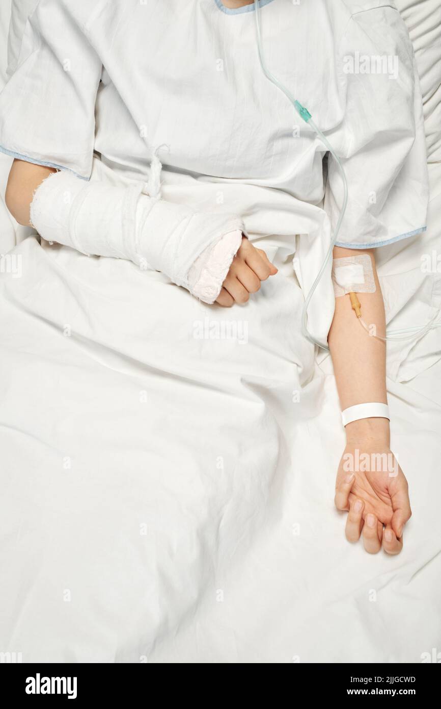 Injection verticale de haut en bas d'une patiente méconnaissable dont le bras est cassé en fonte et qui reçoit des médicaments ou des liquides nutritifs par voie intraveineuse Banque D'Images