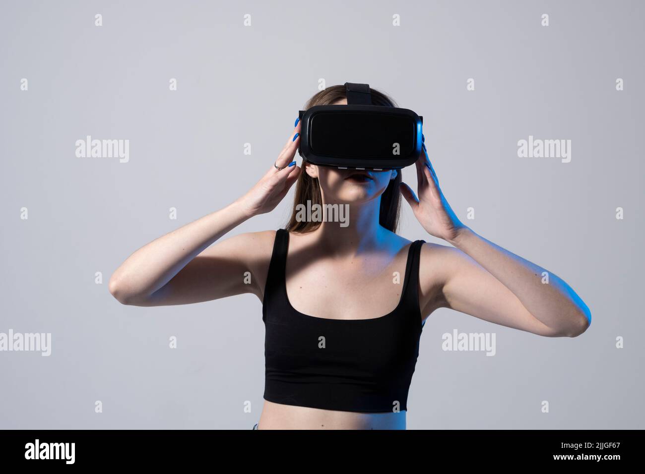 Jolie jolie femme adorable et excitée dans un micro-casque VR regardant et essayant de toucher des objets en réalité virtuelle tout en jouant à un jeu en réalité virtuelle. Banque D'Images