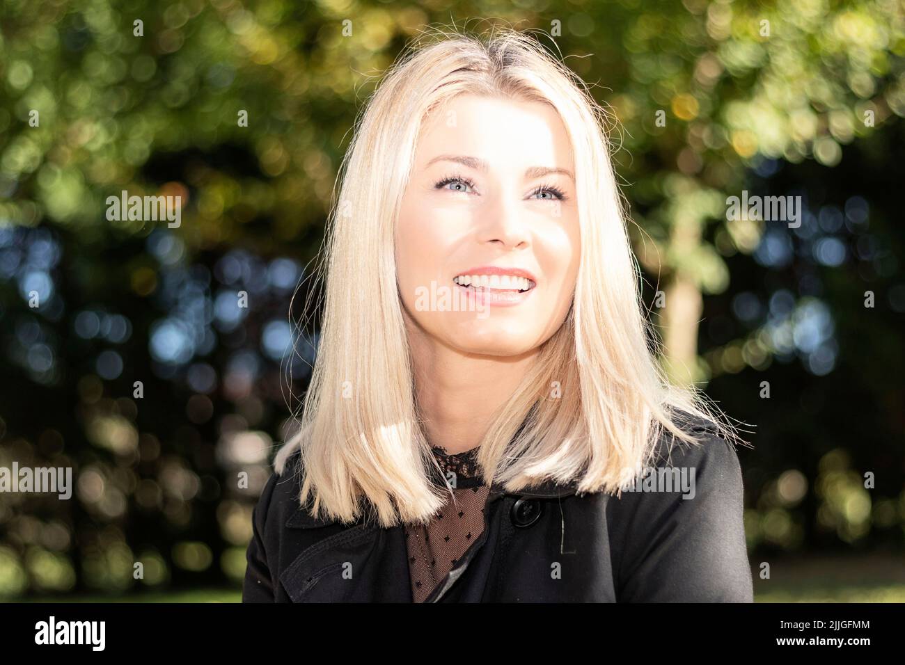 femme blonde souriant dans un parc qui regarde droit devant Banque D'Images