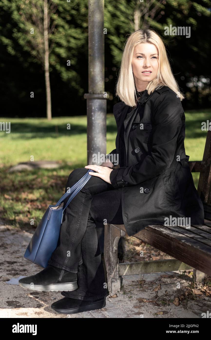 femme blonde pensive en robe noire assise dans un parc Banque D'Images