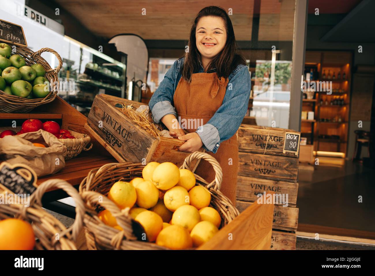 Femme heureuse avec le syndrome de Down souriant en se tenant dans la section des légumes d'une épicerie. Femme habilitée avec un handicap intellectuel wor Banque D'Images