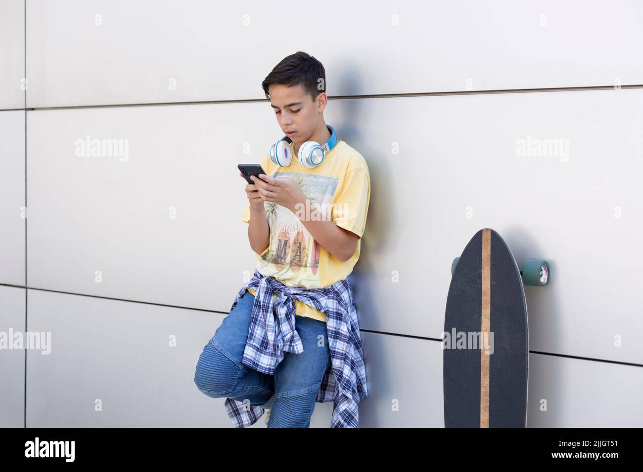 Adolescent du Caucase penché sur un mur à l'aide d'un téléphone portable. Espace pour le texte. Banque D'Images