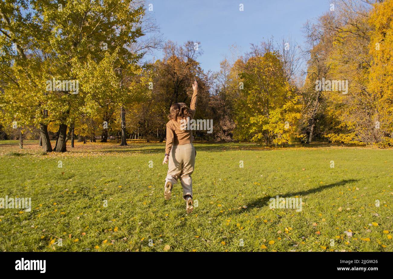 Une jeune femme dans un parc d'automne jouit de la liberté. Elle saute avec les bras vers le haut comme le super-héros Wonder Woman. Banque D'Images