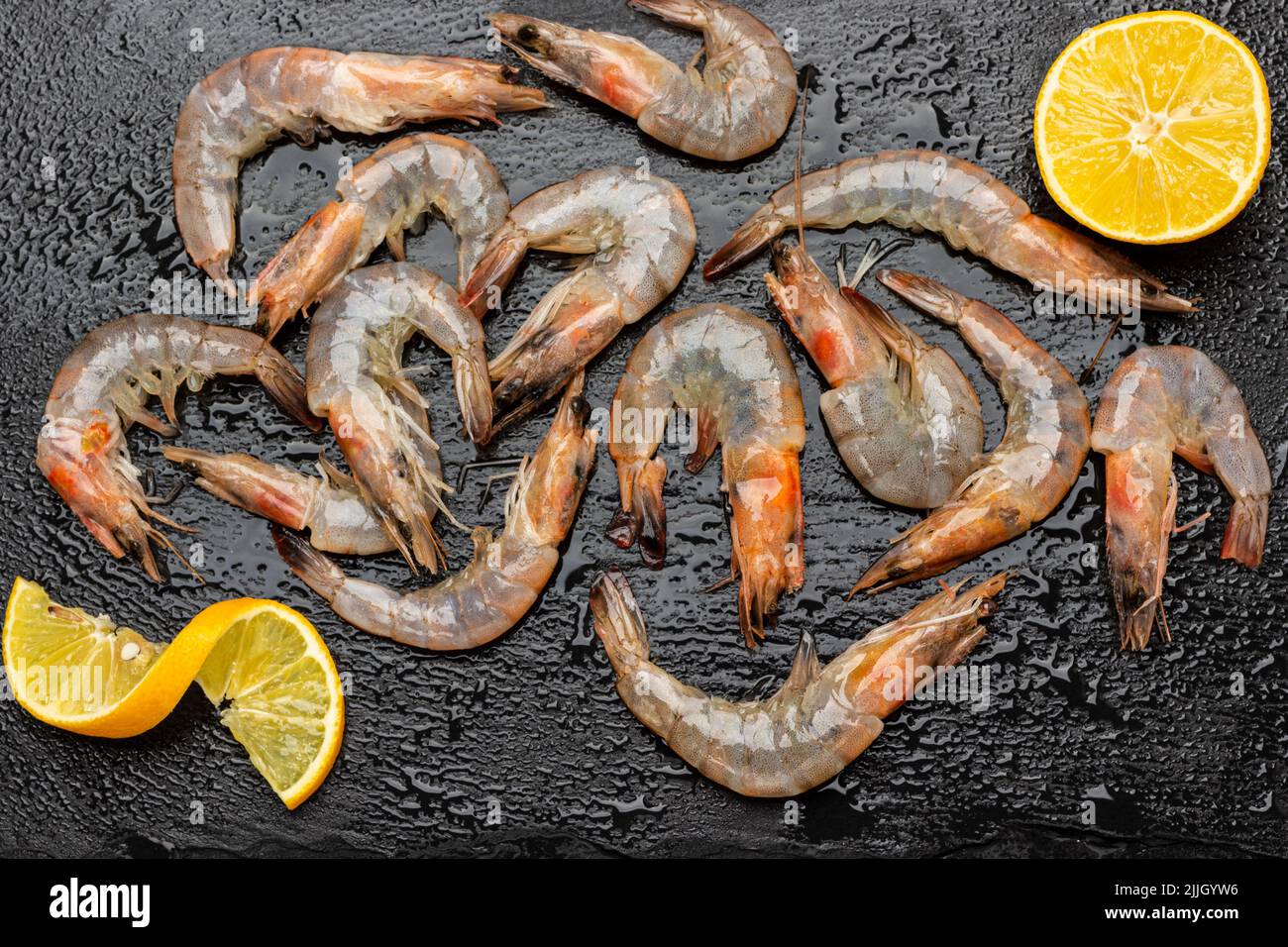 Crevettes et quartiers de citron sur une surface en pierre humide. Pose à plat. Arrière-plan noir Banque D'Images