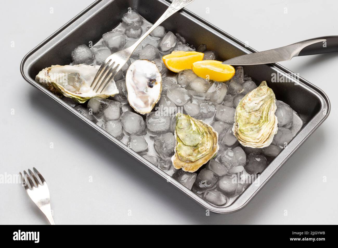 Huîtres en coquilles, citron et glace sur plateau métallique couteau et fourchette sur palette. Pose à plat. Arrière-plan clair Banque D'Images