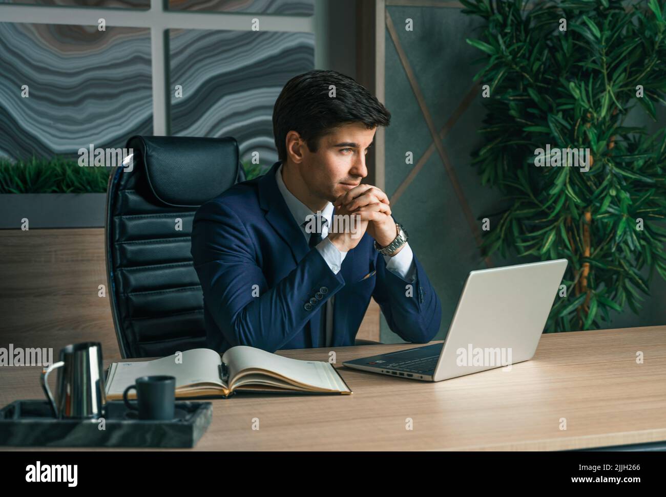 Homme d'affaires travaillant avec un ordinateur portable dans un bureau moderne. Directeur général, pdg. Jeune beau homme confiant en costume assis à table. La leade d'affaires de direction Banque D'Images