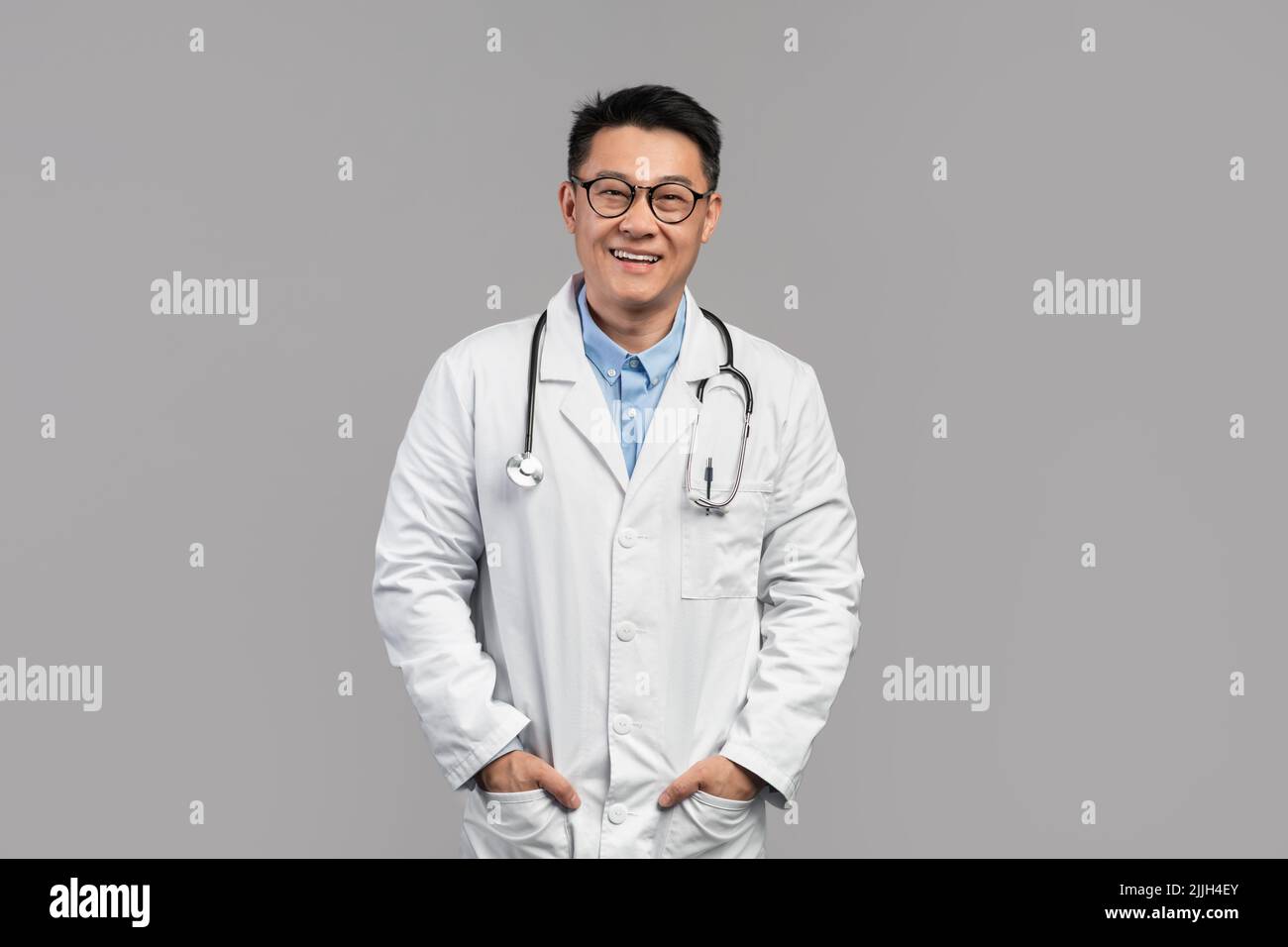 Content confiant attrayant adulte médecin japonais en manteau blanc, lunettes avec stéthoscope regarder la caméra Banque D'Images