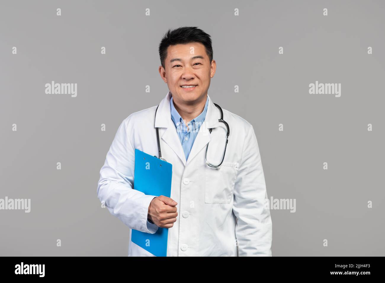 Sourire confiant et mature médecin japonais en manteau blanc avec stéthoscope et tablette regardant la caméra Banque D'Images