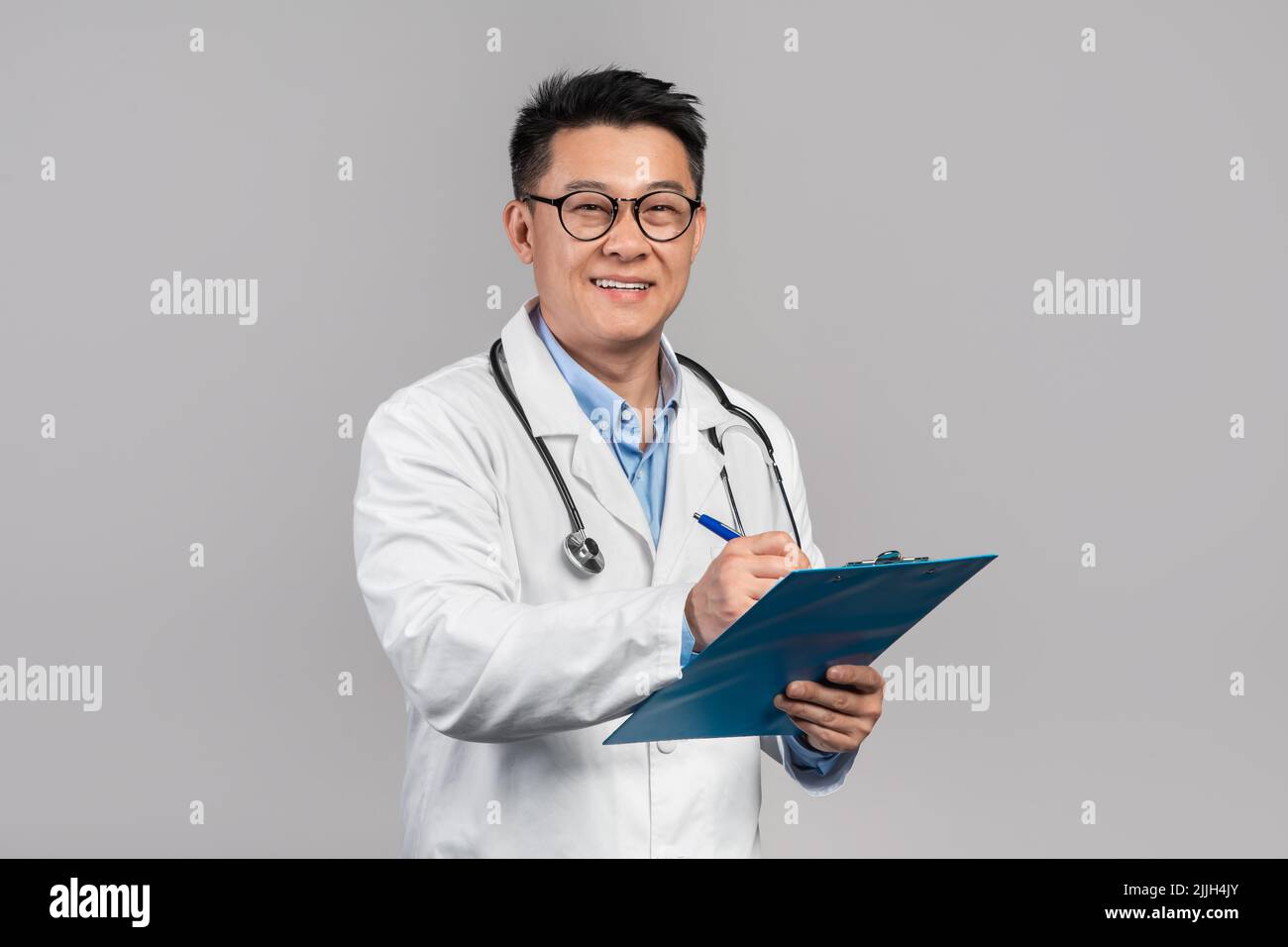 Gai homme coréen mature médecin en manteau blanc, verres avec stéthoscope écrit au comprimé Banque D'Images