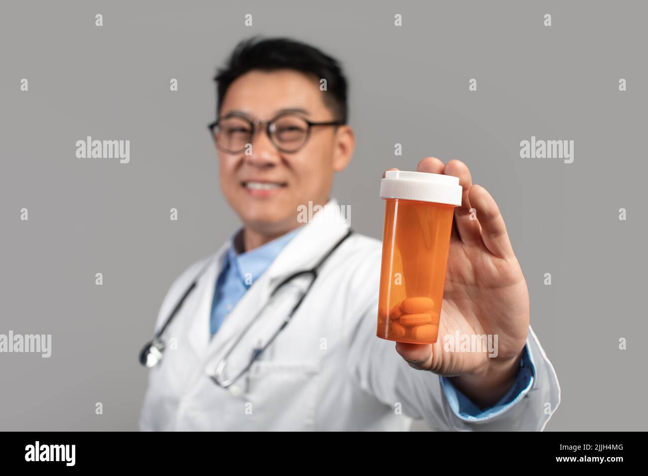 Traitement avec des pilules. Bon médecin chinois adulte dans le manteau blanc et les verres montre bocal de médicaments Banque D'Images