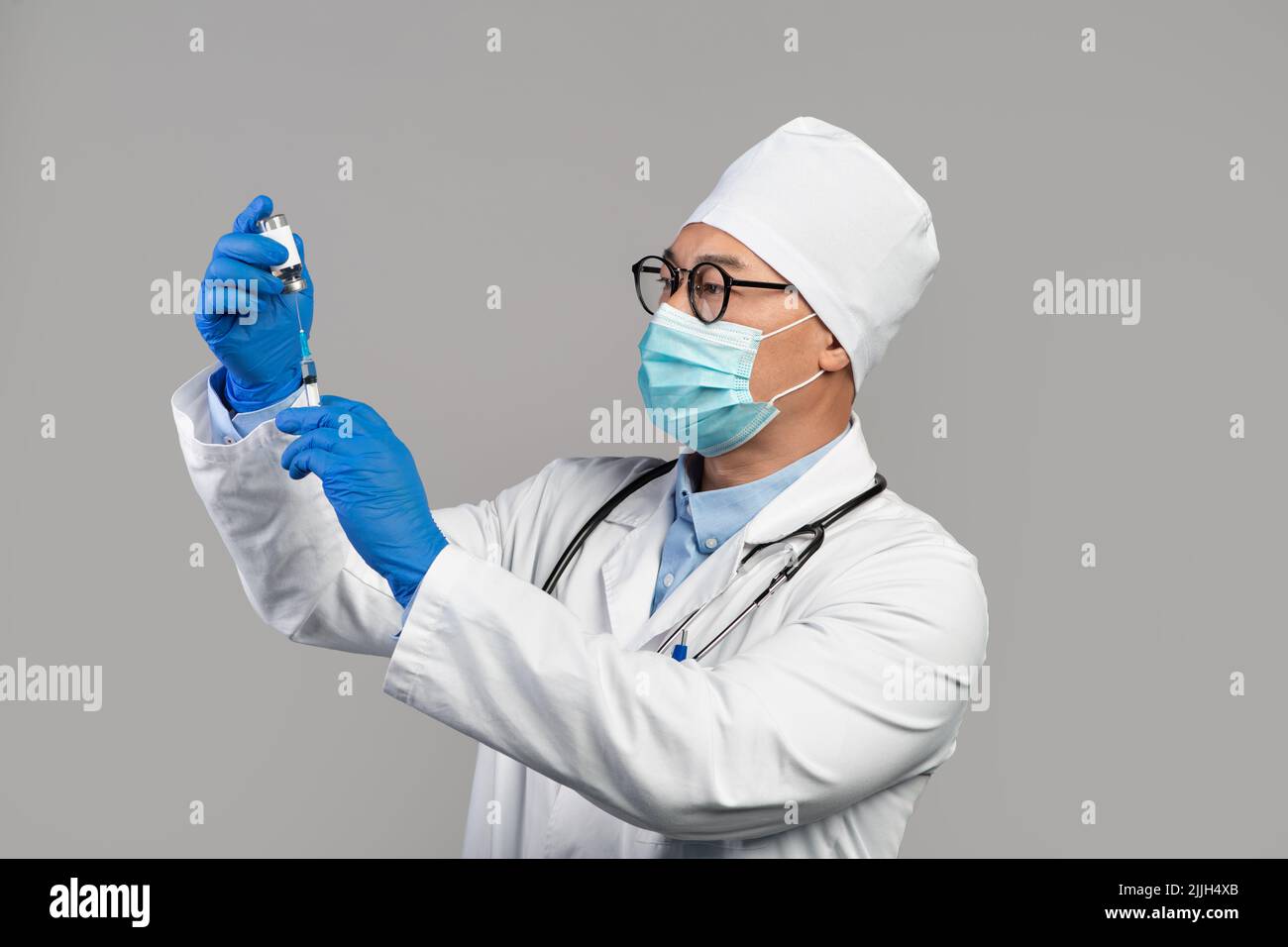 Un médecin coréen adulte sérieux occupé en manteau blanc, des lunettes et des gants prennent le vaccin dans une seringue Banque D'Images