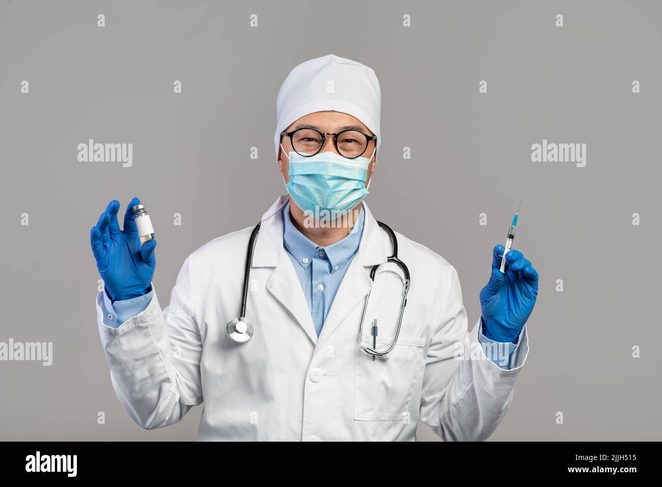 Gai mature médecin chinois en manteau blanc, verres et gants montre le vaccin et la seringue Banque D'Images