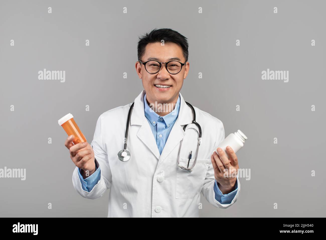 Un homme coréen heureux adulte thérapeute en manteau blanc et verres montre des bocaux avec des pilules Banque D'Images