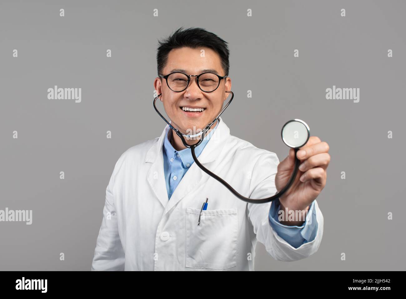 Gai confiant et confiant médecin japonais mature en manteau blanc et des lunettes écoute caméra avec stéthoscope Banque D'Images
