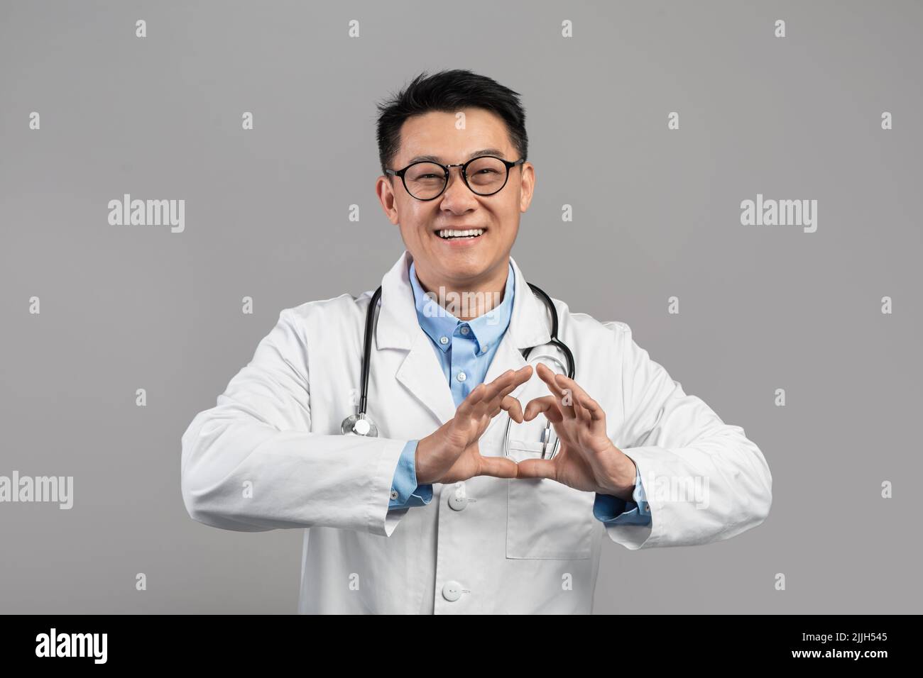 Joyeux médecin japonais d'âge moyen en manteau blanc et des lunettes montre le coeur avec les mains isolées Banque D'Images