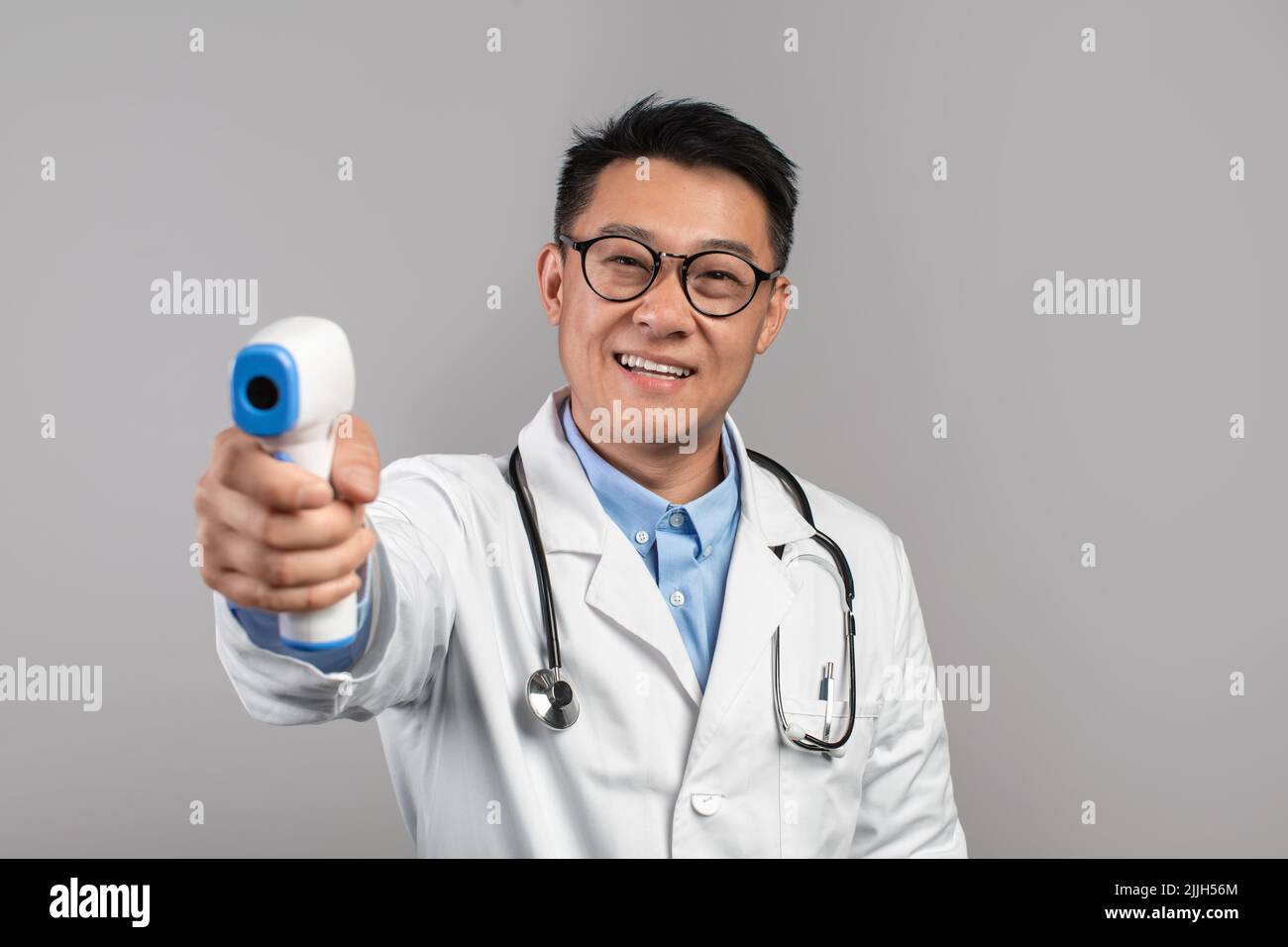 Joyeux adulte asiatique homme médecin en manteau blanc, verres mesure la température avec thermomètre infrarouge Banque D'Images