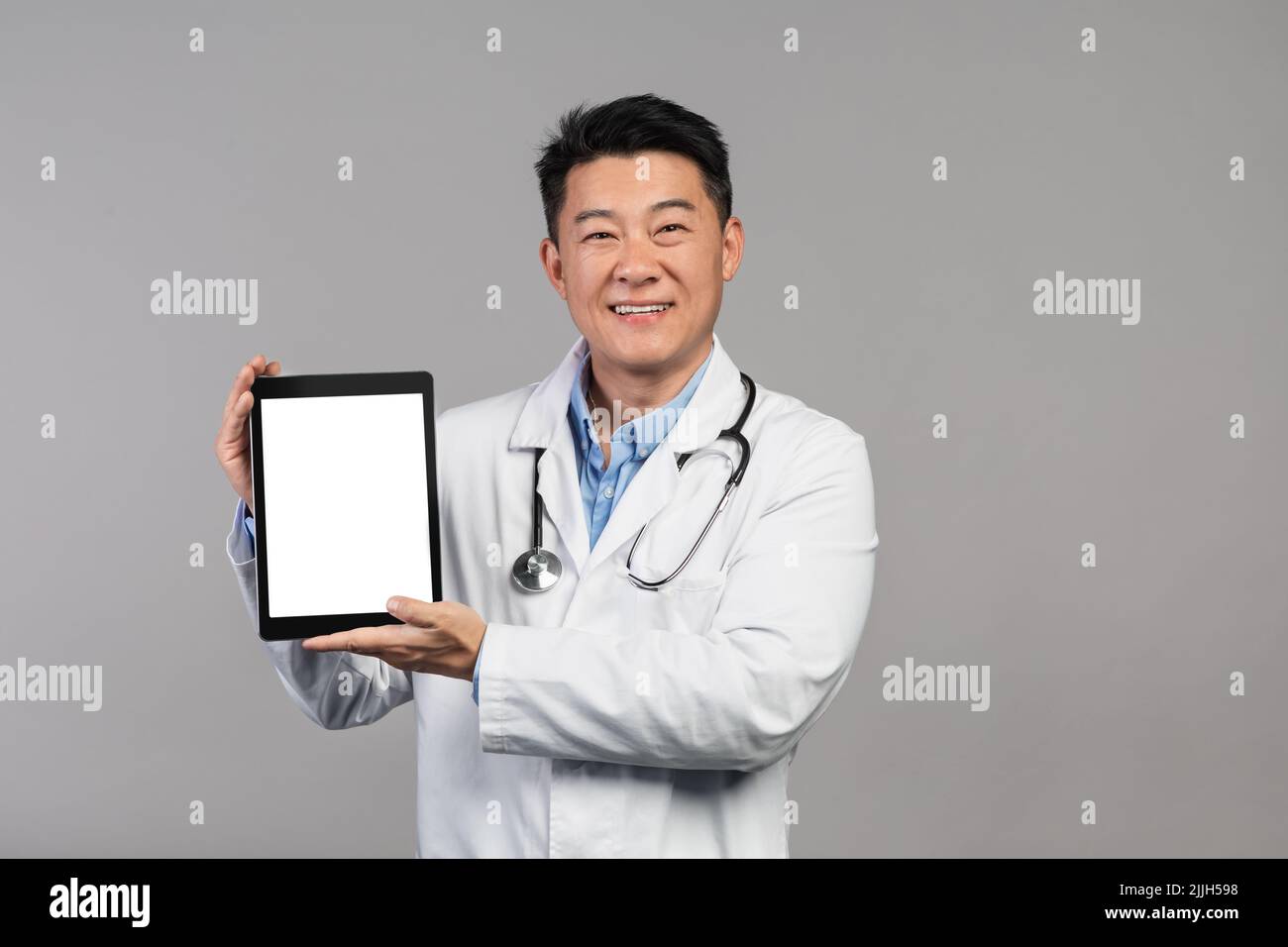Sourire mature médecin chinois en manteau blanc avec stéthoscope montrant un comprimé avec écran blanc Banque D'Images